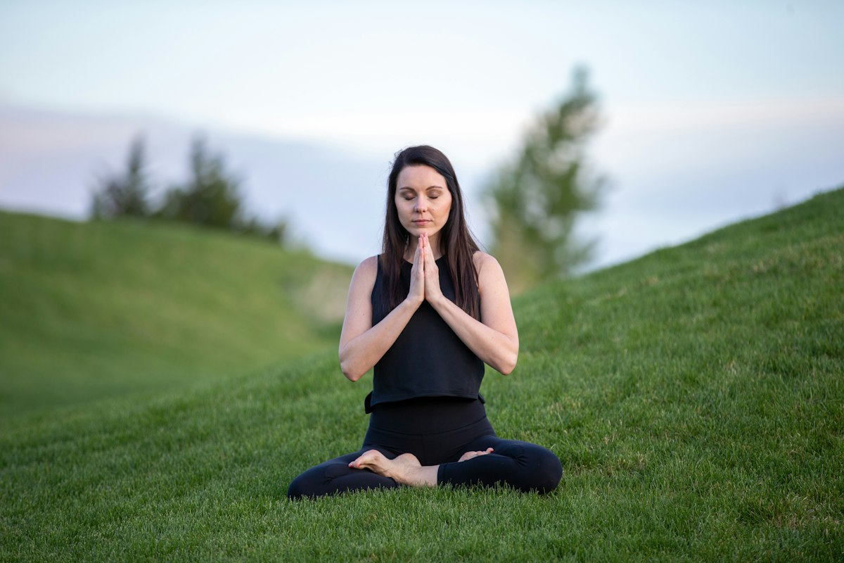 Mujer meditando sentada sobre el césped en un entorno natural